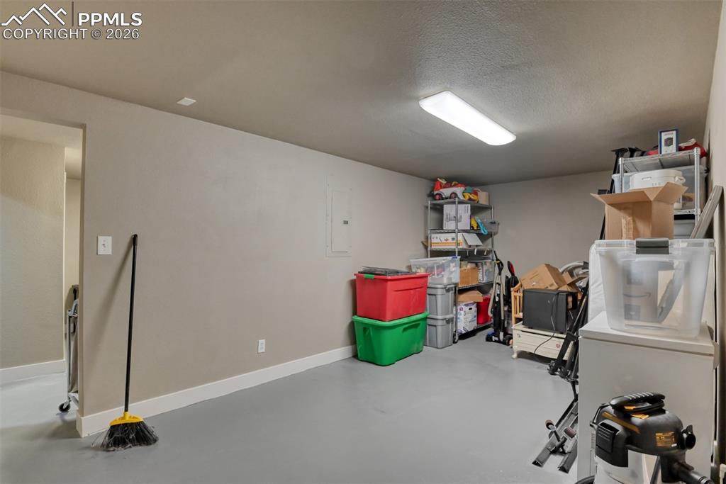 Image 35 of 50: Basement with white fridge, electric panel, and a textured ceiling
