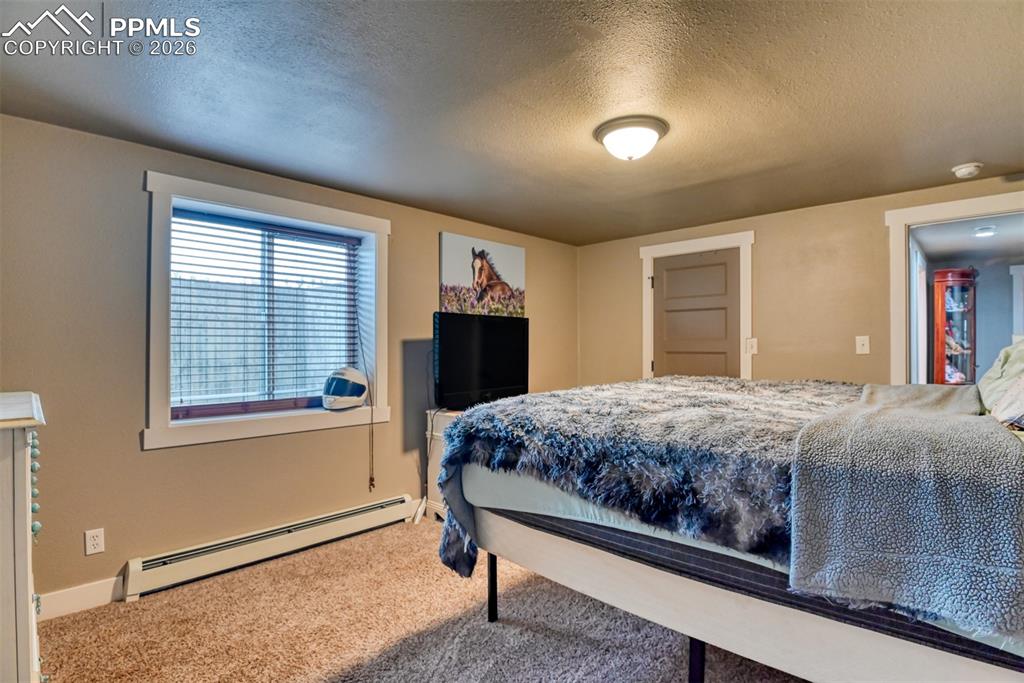 Image 36 of 50: Carpeted bedroom with baseboard heating and a textured ceiling