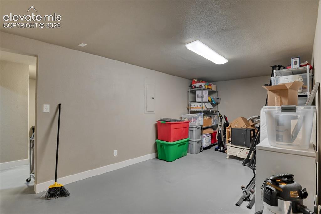 Image 36 of 50: Basement with white fridge, electric panel, and a textured ceiling
