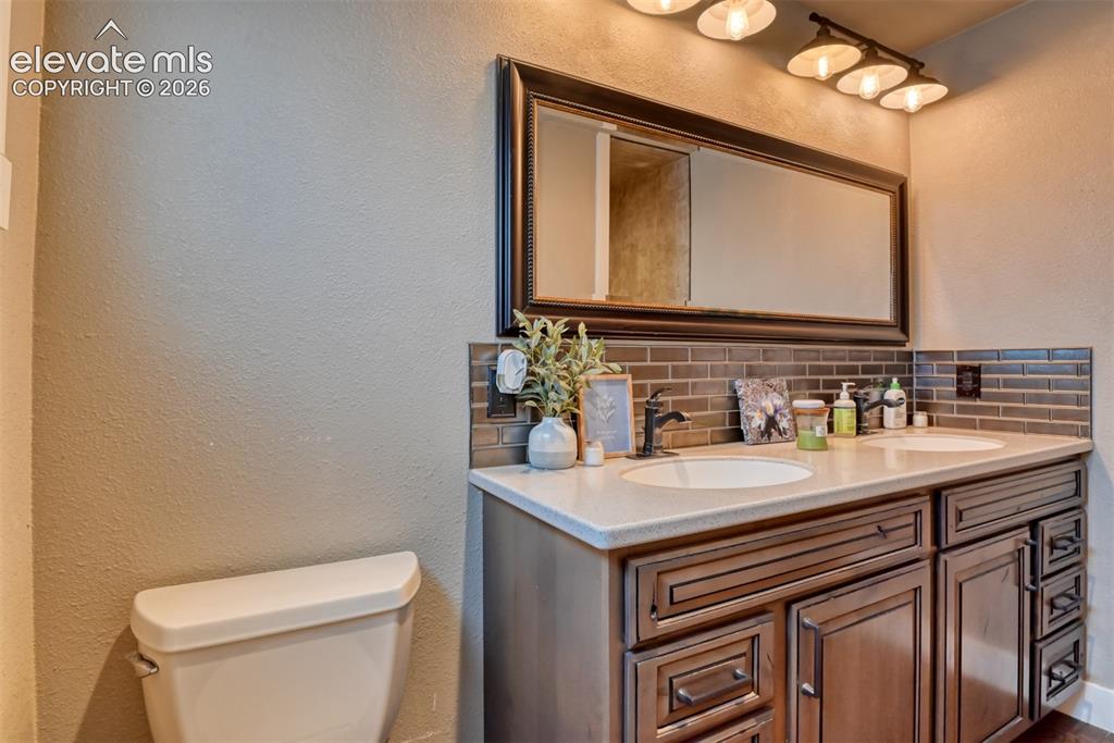 Image 42 of 50: Full bath featuring a textured wall, double vanity, and decorative backspla