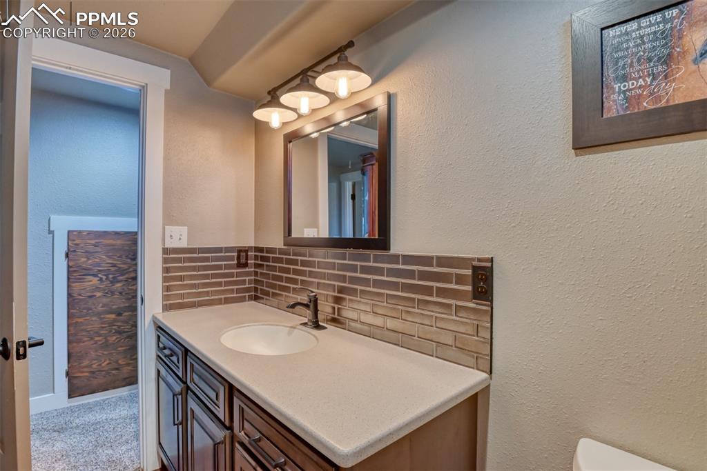 Image 43 of 50: Bathroom featuring decorative backsplash, a textured wall, and vanity