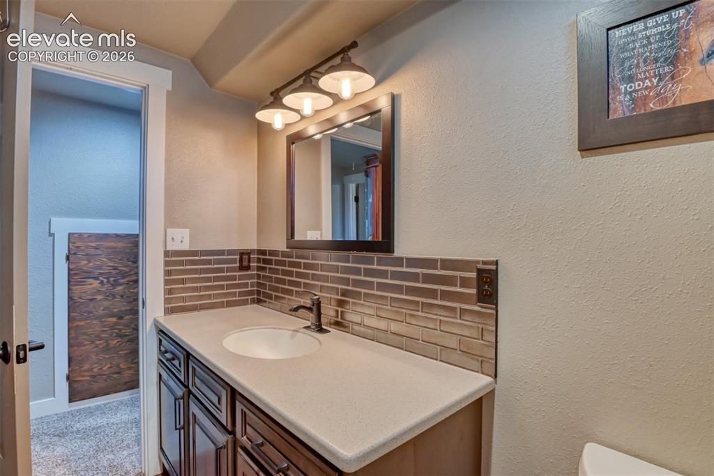 Image 44 of 50: Bathroom featuring decorative backsplash, a textured wall, and vanity
