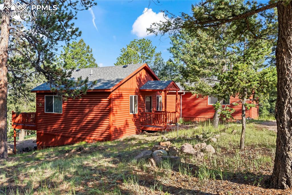 Caption: View of side of property with a wooden deck, roof with shingles, and faux log siding