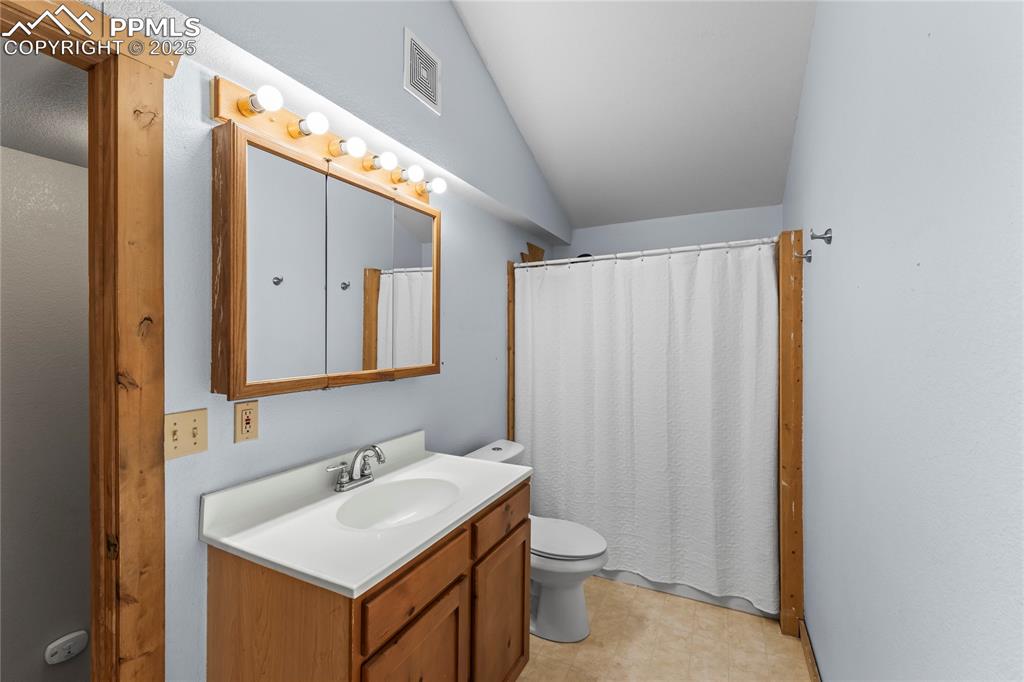 Image 18 of 39: Bathroom with vanity, vaulted ceiling, and curtained shower