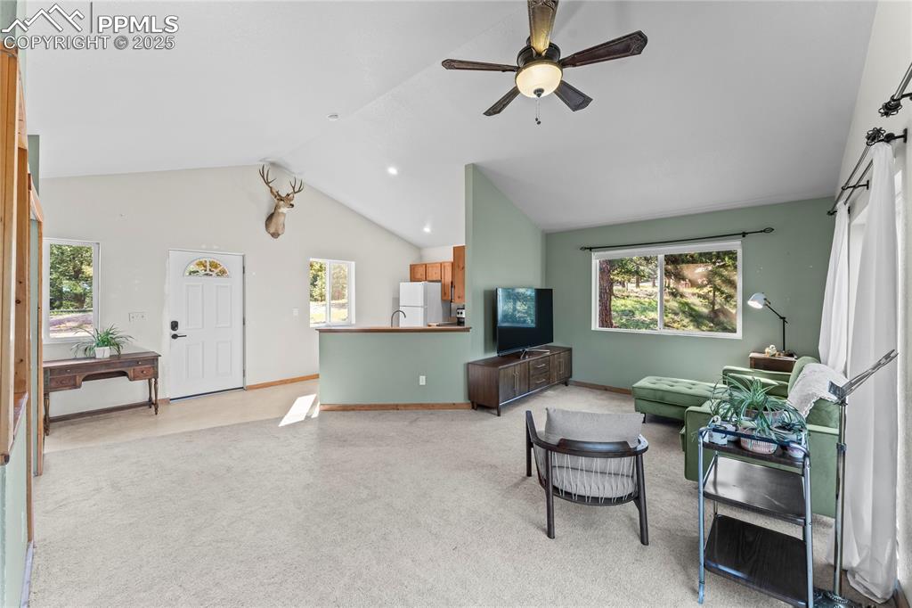 Image 9 of 39: Living area with light carpet, ceiling fan, and high vaulted ceiling