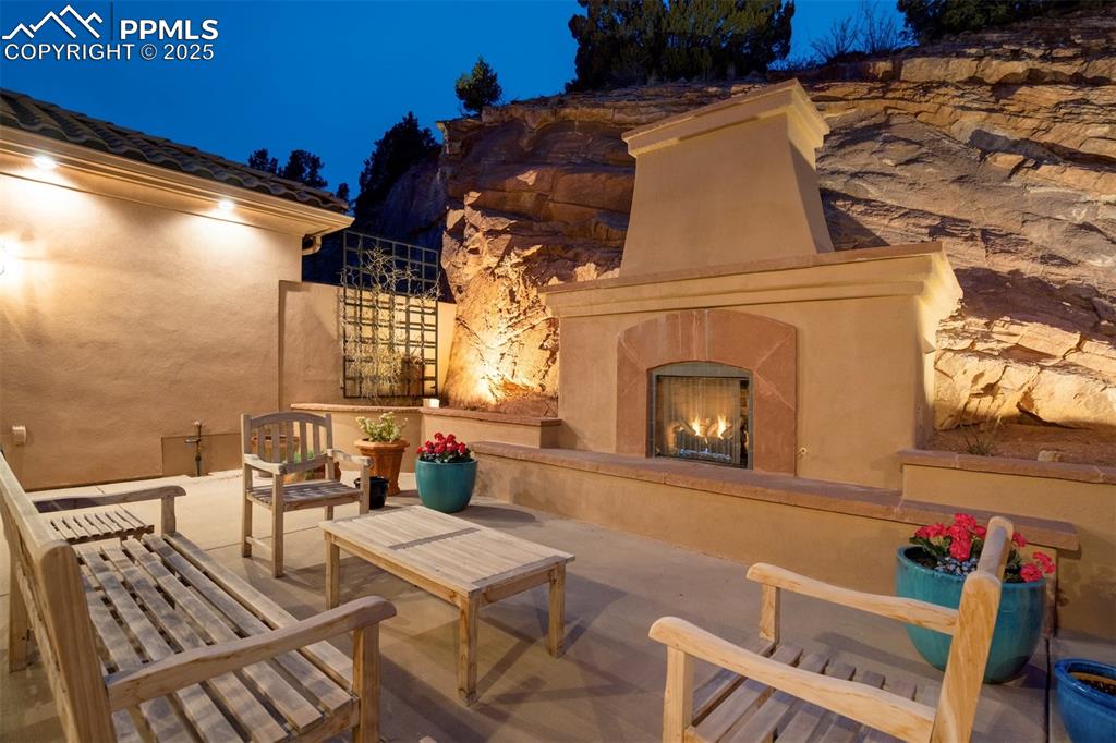 Image 42 of 50: Main patio with gas fireplace, large seating area & evening accent lighting