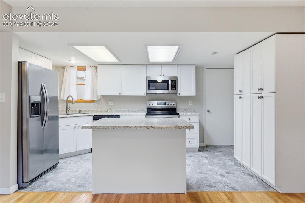 Image 15 of 50: Kitchen featuring white cabinetry, stainless steel appliances, a center isl