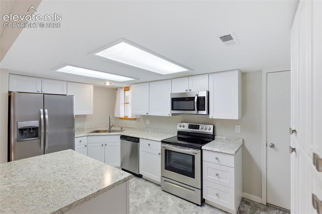 Image 16 of 50: Kitchen featuring stainless steel appliances, white cabinetry, light-toned
