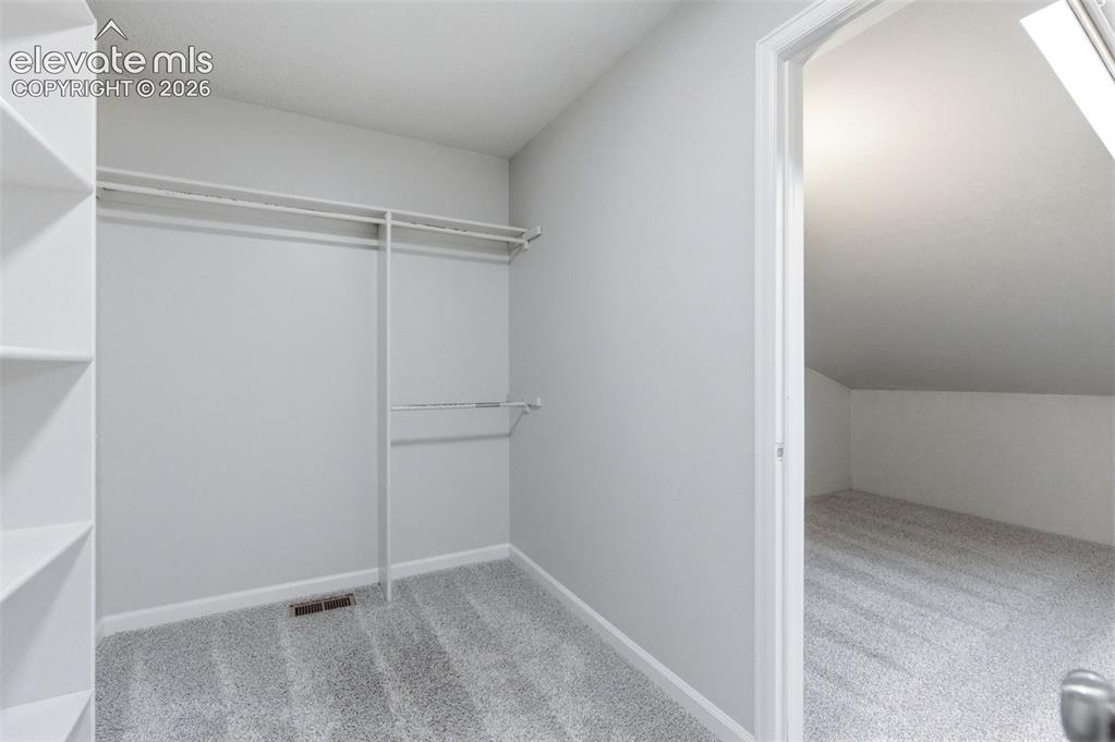 Image 32 of 50: Walk-in closet with built-in shelving, two hanging rods, and light-grey car