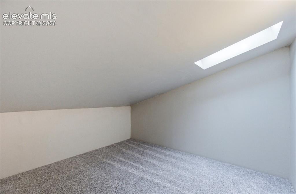 Image 34 of 50: Room with a vaulted ceiling and skylight, featuring light gray carpeting an
