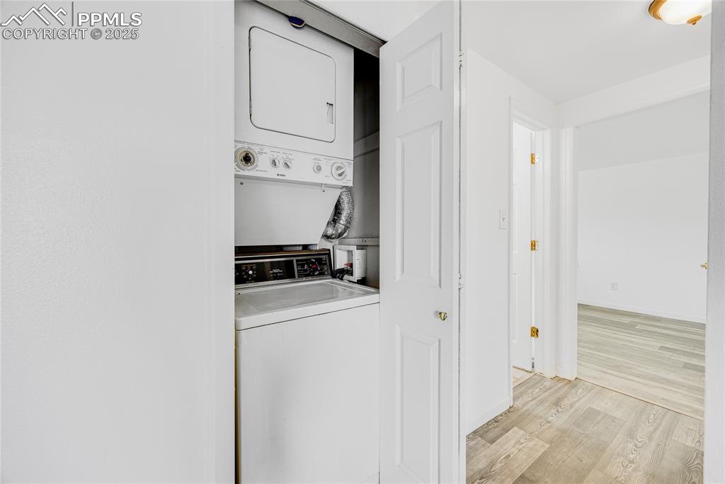 Image 11 of 24: Laundry room with light wood-style flooring and stacked washer / dryer