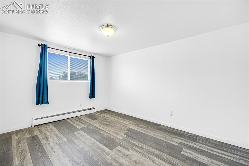 Image 15 of 24: Empty room with a baseboard heating unit and light wood finished floors