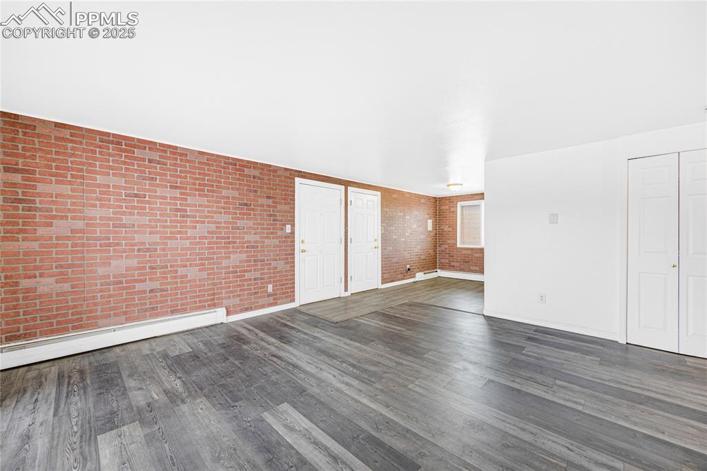 Image 6 of 24: Unfurnished living room featuring dark wood-type flooring, brick wall, and 