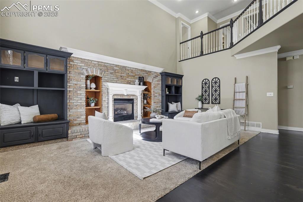 Image 11 of 44: Living area with a high ceiling, ornamental molding, built in shelves, a fi