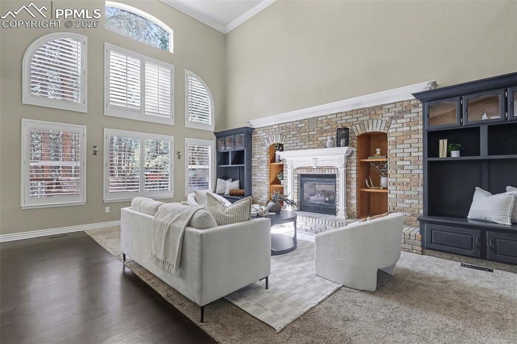 Image 12 of 44: Carpeted living area featuring a high ceiling, built in shelves, a fireplac
