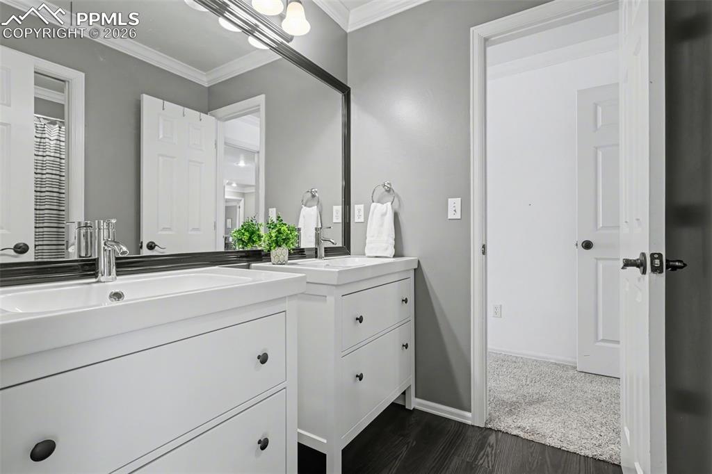 Image 26 of 44: Full bath with two vanities, ornamental molding, and dark wood-type floorin