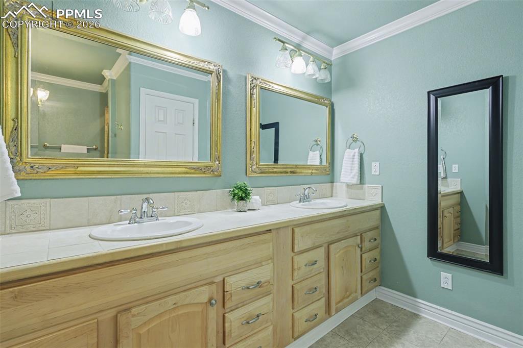 Image 29 of 44: basement Bathroom featuring crown molding, double vanity, and light tile pa