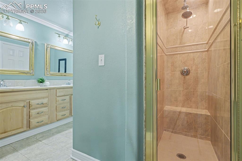 Image 30 of 44: basement Full bathroom with double vanity, a stall shower, and light tile p