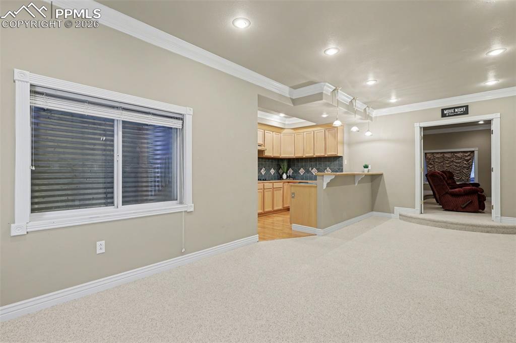 Image 31 of 44: Basement Kitchen area with light wood finish cabinetry, light carpet, ornam