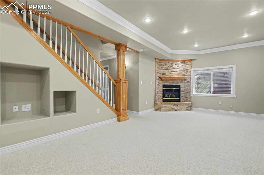 Image 32 of 44: Basement living room with crown molding, light carpet, a stone fireplace, a