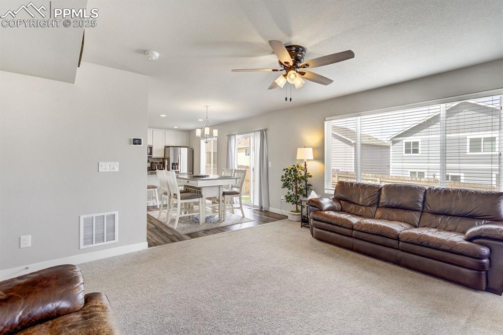 Image 10 of 50: Living area featuring carpet, visible vents, baseboards, and ceiling fan wi