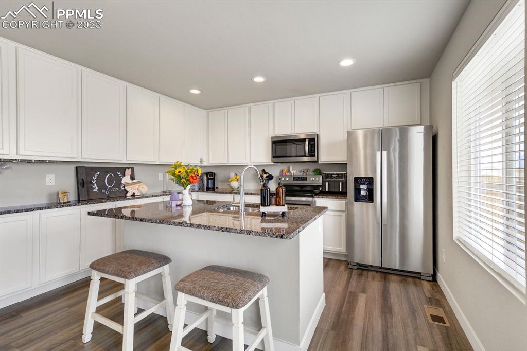 Image 14 of 50: Kitchen featuring dark stone counters, stainless steel appliances, white ca