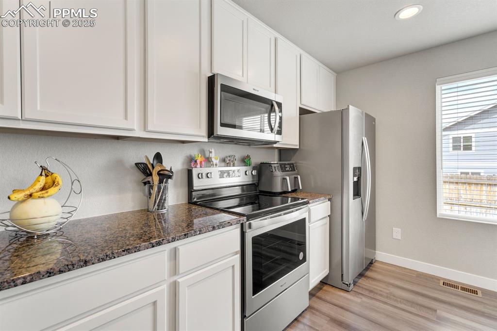 Image 16 of 50: Kitchen with white cabinets, recessed lighting, stainless steel appliances,