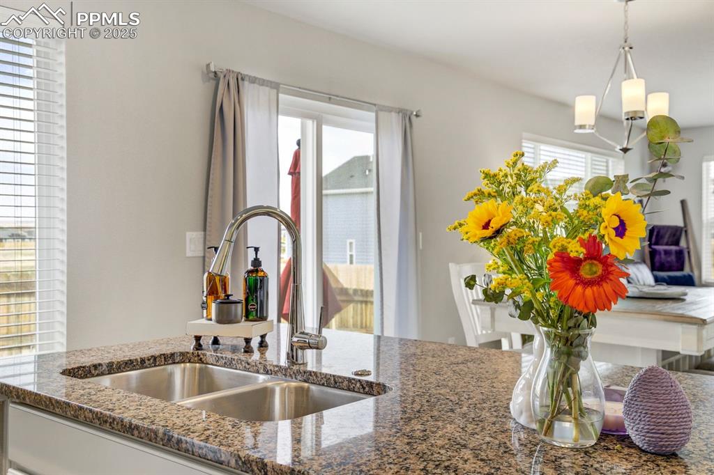 Image 19 of 50: Kitchen with decorative light fixtures, a sink, and dark stone counters