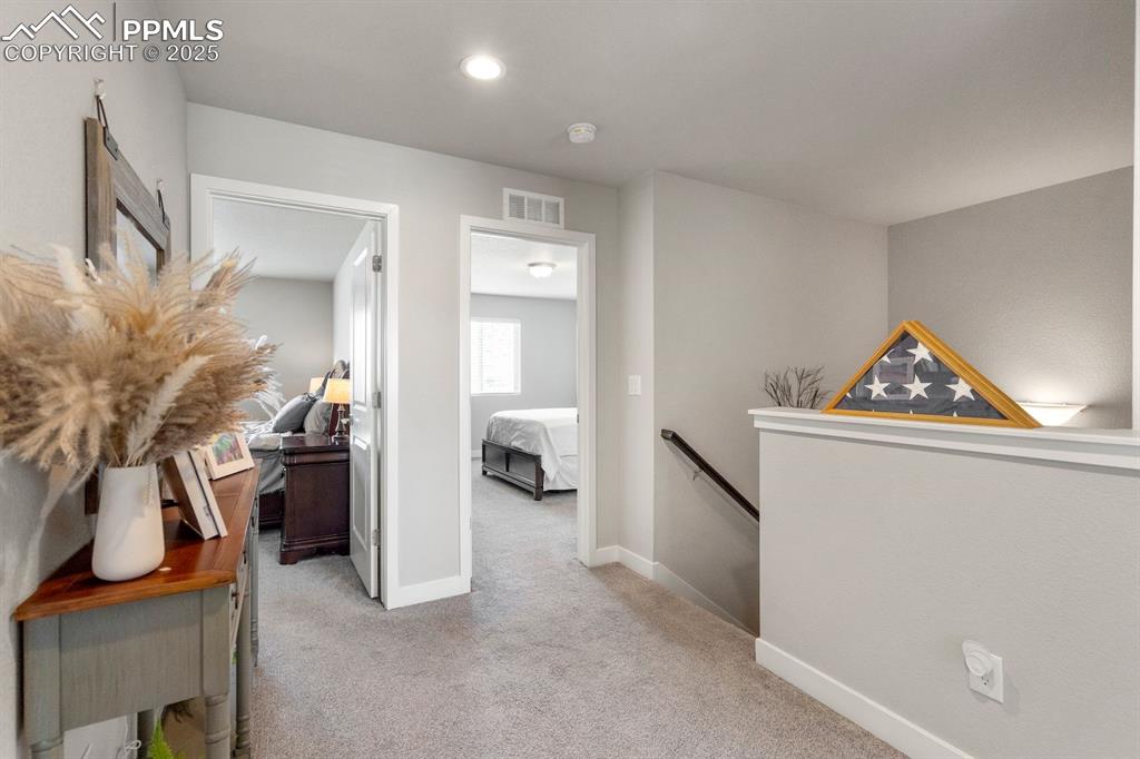 Image 21 of 50: Hallway with an upstairs landing, carpet floors, baseboards, visible vents,