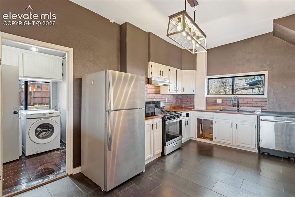 Image 10 of 35: Kitchen featuring white cabinetry, brick backsplash, and wood-finish floori