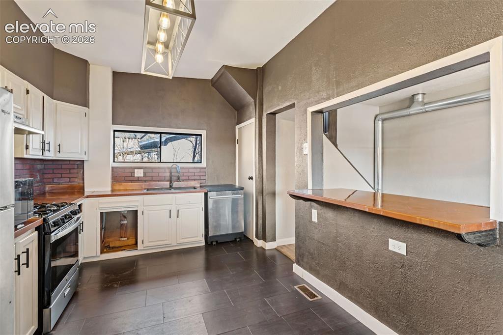 Image 11 of 35: Kitchen featuring a gas range, white cabinetry with dark hardware, brick ba