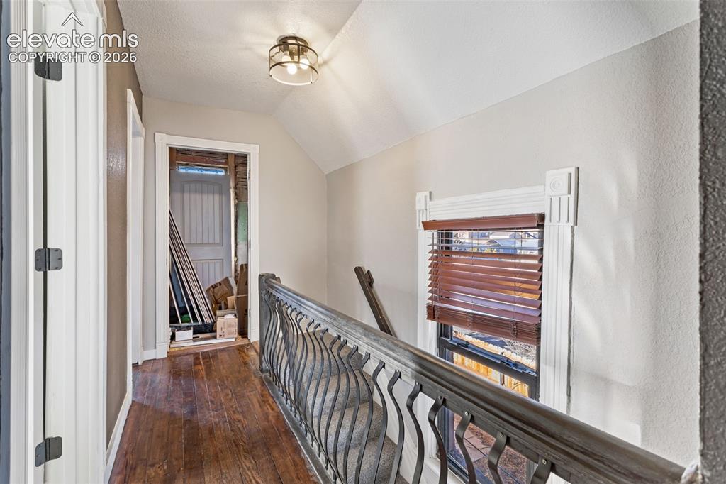 Image 16 of 35: Hallway featuring rich wood-finish flooring, an ornate metal railing, and a