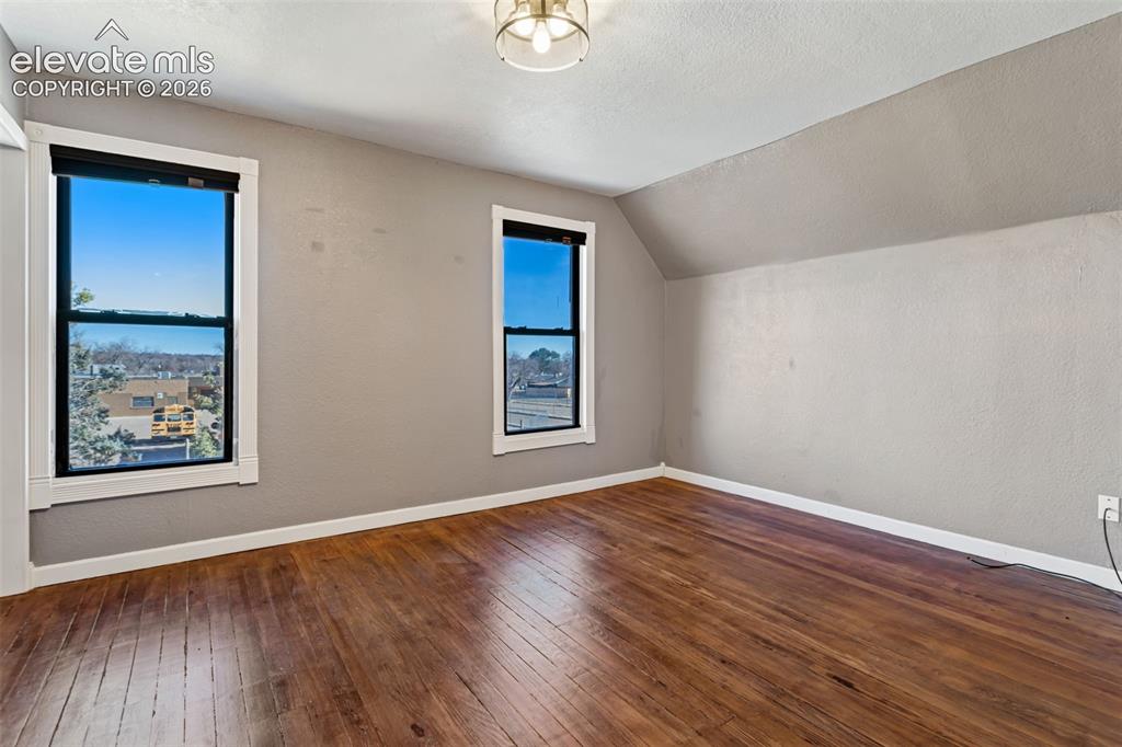Image 18 of 35: Hardwood flooring complements light gray walls in this room with two window