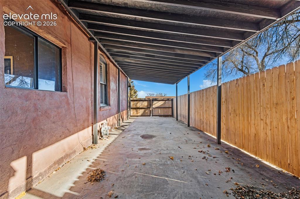 Image 26 of 35: Covered carport or patio area featuring a concrete slab, wood privacy fence