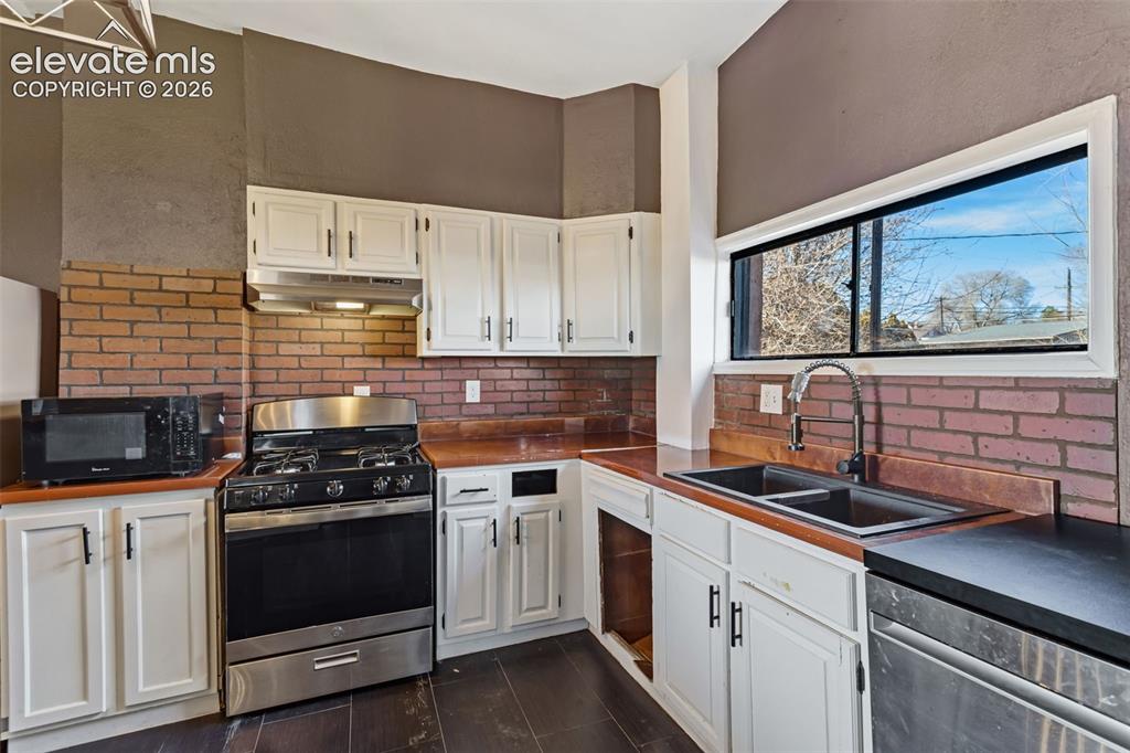 Image 8 of 35: Kitchen featuring white cabinetry, brick backsplash, stainless steel applia