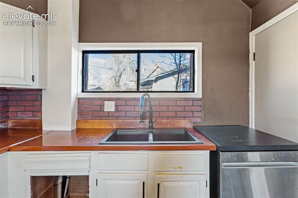 Image 9 of 35: Kitchen area featuring a double-basin sink with a gooseneck faucet, brick b