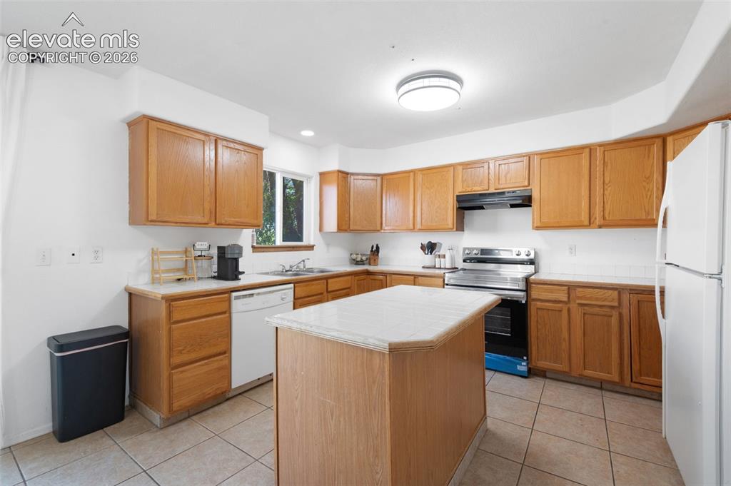 Image 9 of 31: Kitchen with wood-finish cabinetry, tile flooring, and a central island wit