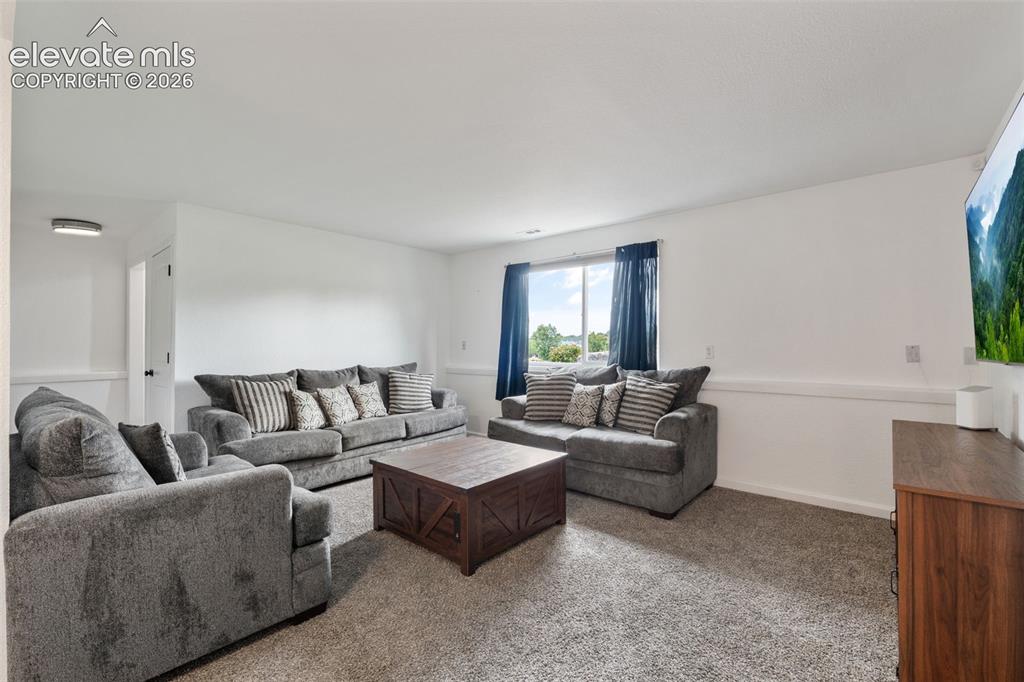 Image 23 of 43: Spacious living area featuring neutral carpeting, white walls, and a large 