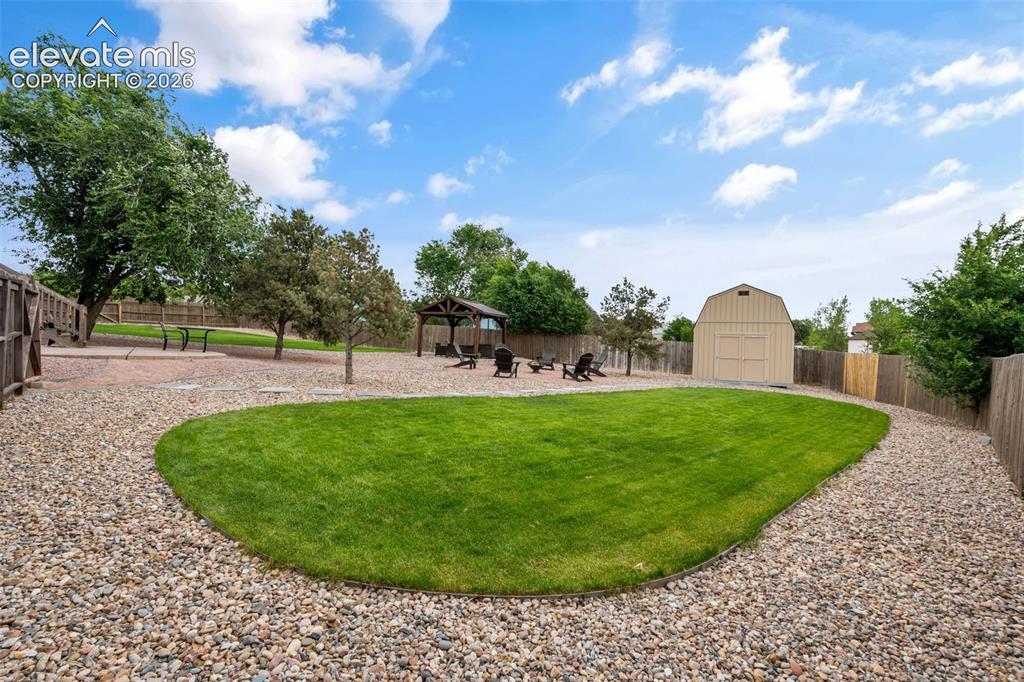 Image 32 of 43: Expansive backyard featuring a central lawn area, gravel pathways, a dedica