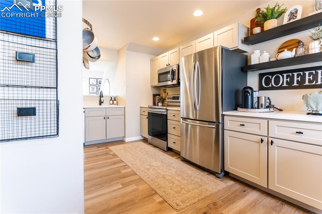 Image 9 of 23: Kitchen with stainless steel appliances, open shelves, light wood-style flo