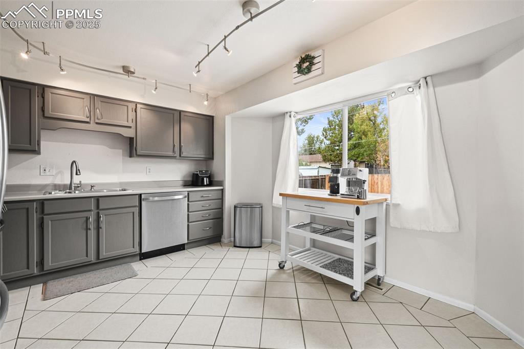 Image 9 of 33: Kitchen with light countertops, gray cabinetry, dishwasher, and light tile 