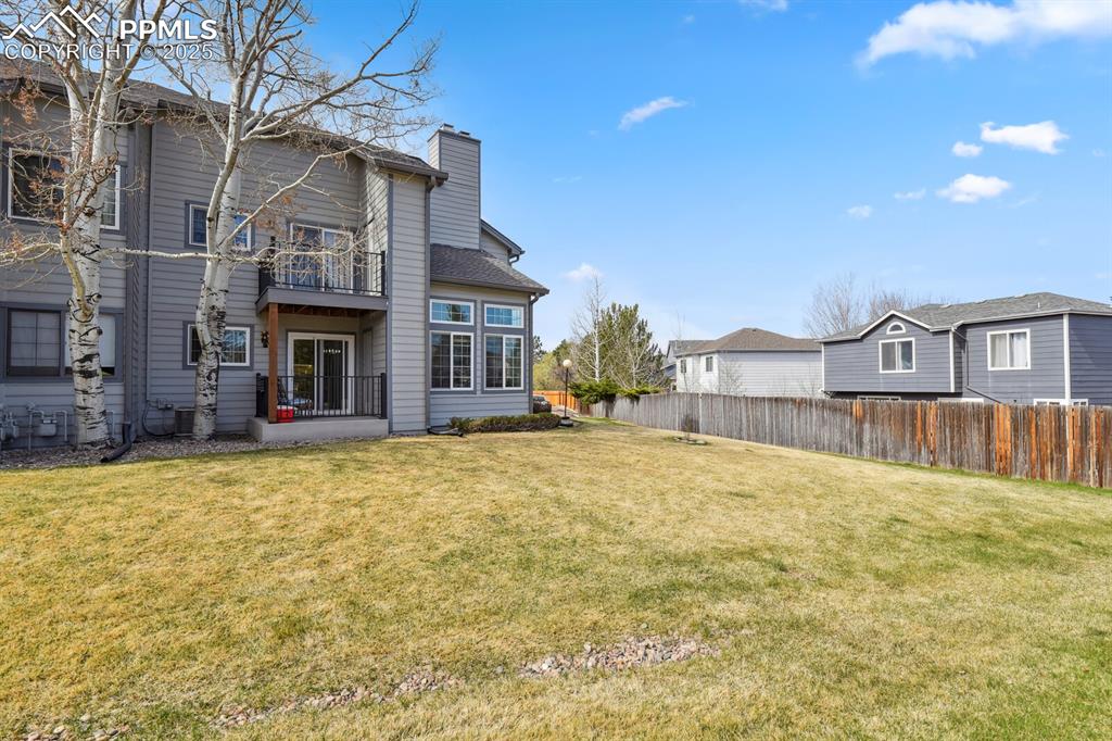 Caption: Rear view of house with a balcony, fence, and a lawn