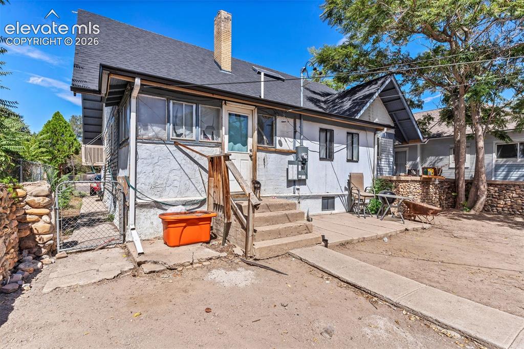 Image 29 of 31: Rear exterior featuring a concrete patio, wood steps, and a chain-link fenc
