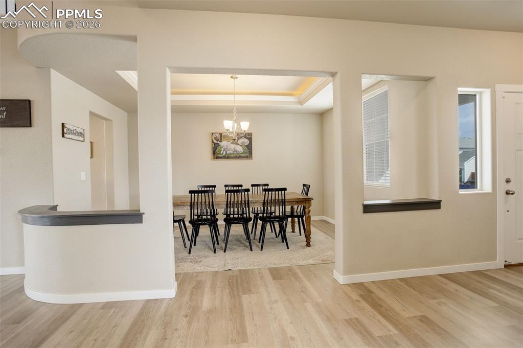 Image 33 of 50: Dining area featuring light wood-style floors, a chandelier, and a raised c