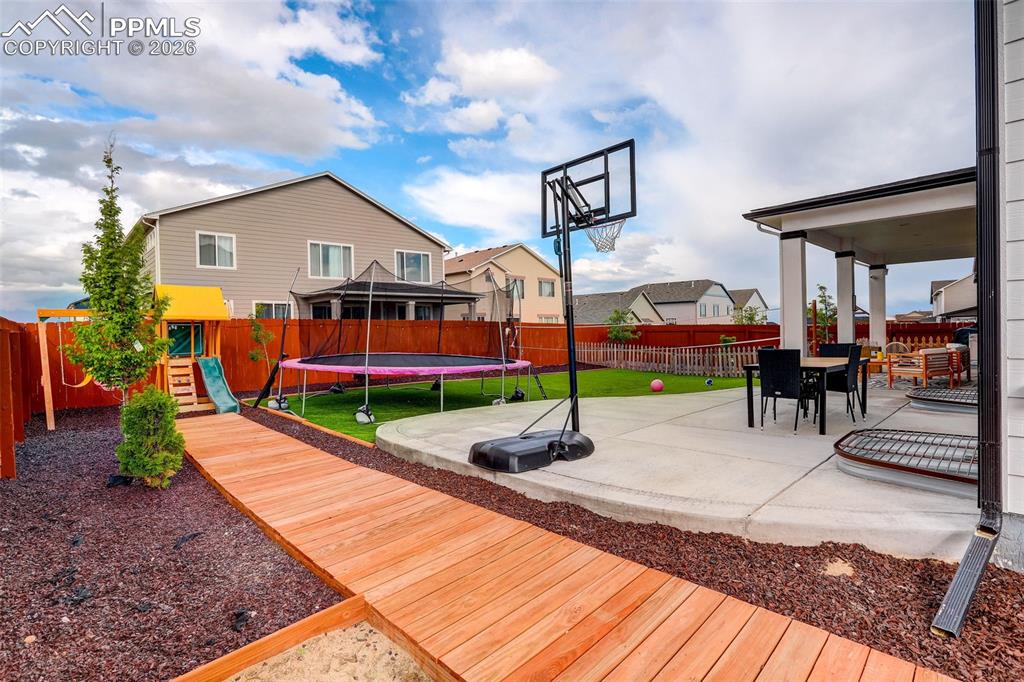 Image 46 of 50: Deck with a playground, a trampoline, a patio, and a fenced backyard