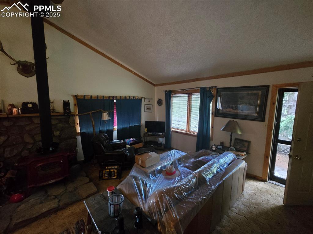 Image 6 of 23: Carpeted living room featuring a wood stove, lofted ceiling, and a textured