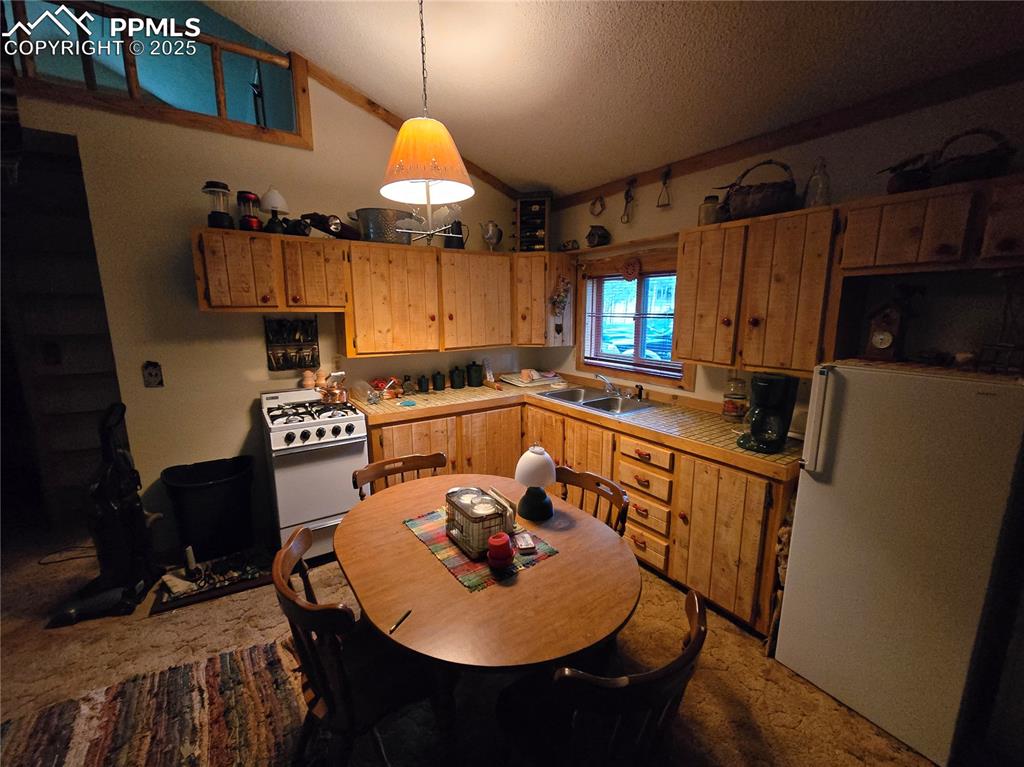 Image 7 of 23: Kitchen featuring tile countertops, white appliances, vaulted ceiling, carp