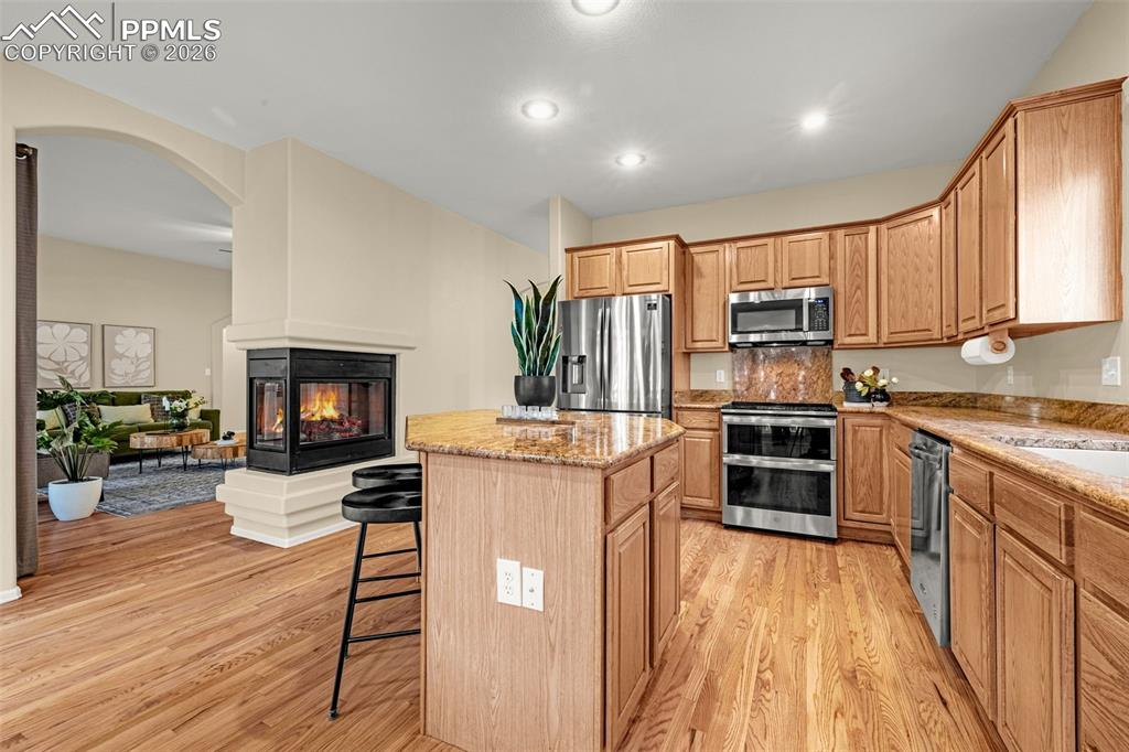 Image 13 of 40: Kitchen featuring hardwood floors, a stone fireplace, stainless steel appli