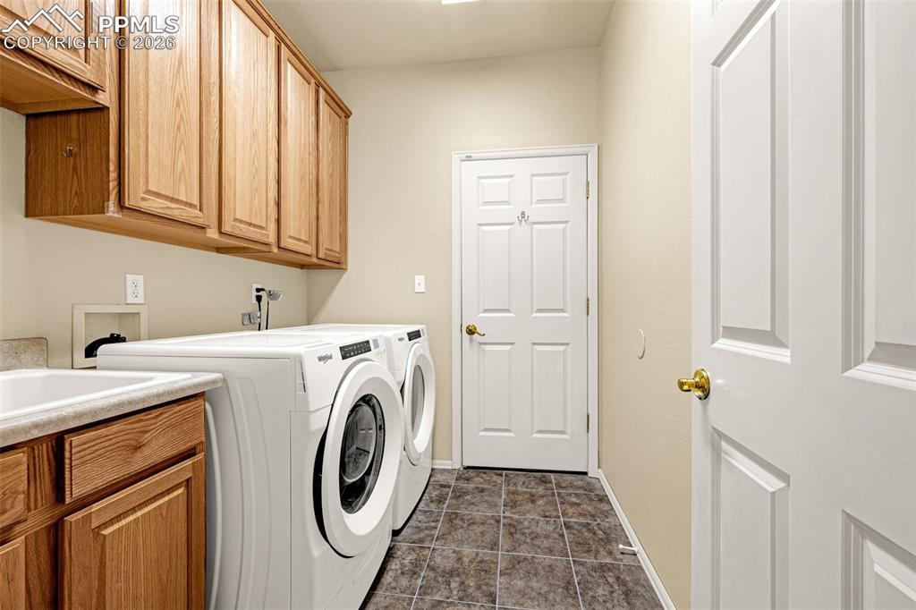 Image 16 of 40: This utility space features a sink with a countertop, wood cabinetry, and t