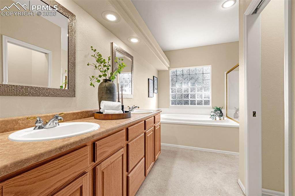 Image 21 of 40: Bathroom featuring a double vanity with wooden cabinetry, a built-in bathtu